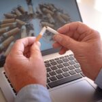 Adult hands holding a broken cigarette over laptop keyboard, ready stop smoking. World tuberculosis day, world no tobacco day, corona virus covid-19, biological air pollution; organ donation concept