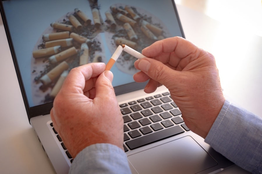 Adult hands holding a broken cigarette over laptop keyboard, ready stop smoking. World tuberculosis day, world no tobacco day, corona virus covid-19, biological air pollution; organ donation concept